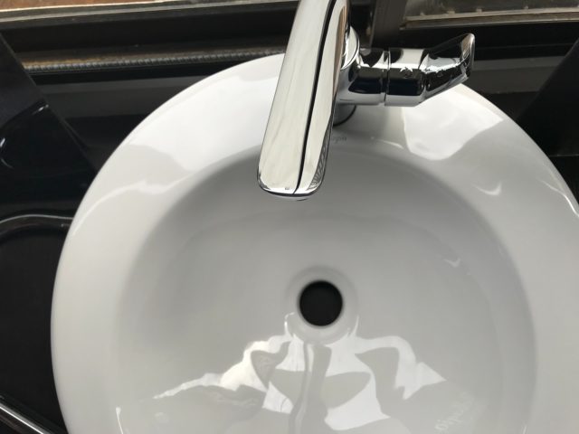 White porcelain round sink with silver faucet viewed from above.