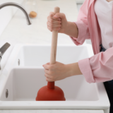 A person using a plunger to unclog a kitchen sink.