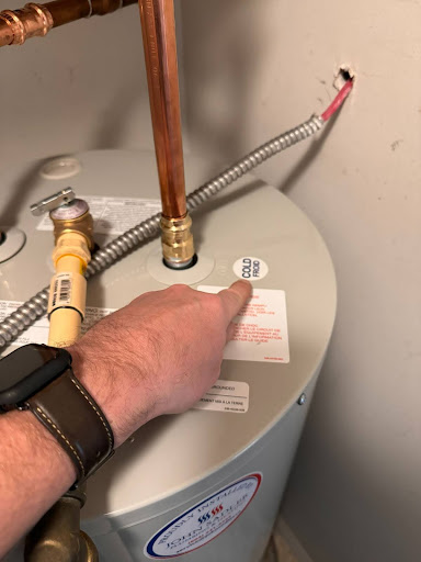 A hand pointing to the label indicating a cold-water pipe on a hot water tank.