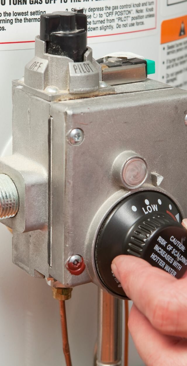 turning-down Hand turning thermostat dial on a water heater.